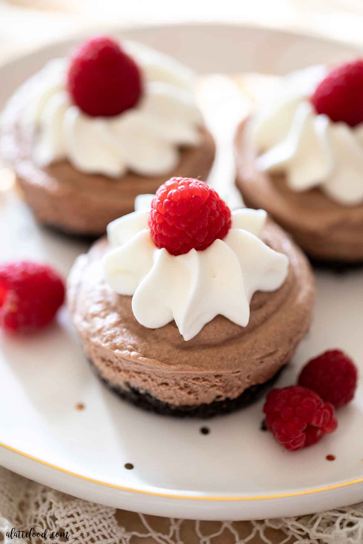 mini no bake chocolate cream pies with whipped cream, cream cheese, and fresh raspberries on a white dessert plate.